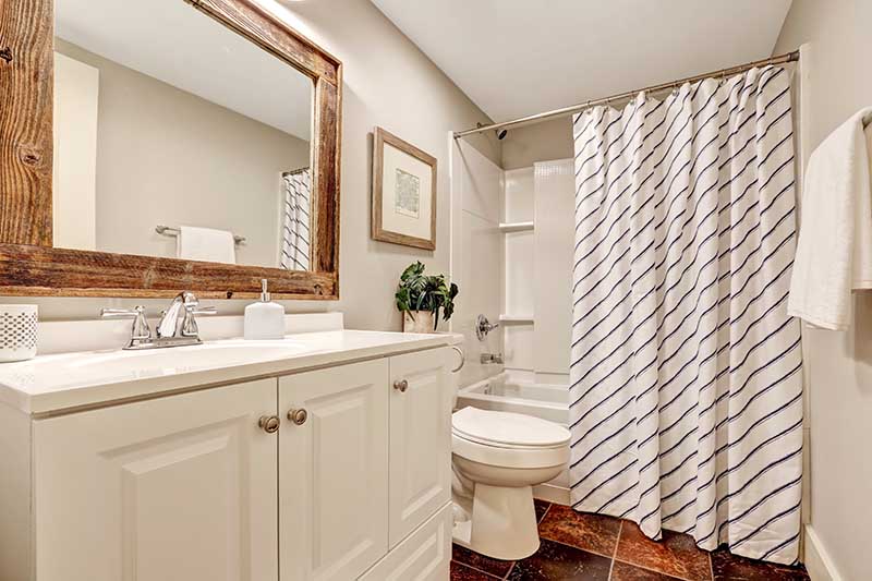 White tones Bathroom with vanity cabinet and wooden framed mirror. Decorated with picture, plant pot and striped curtain. Northwest, USA